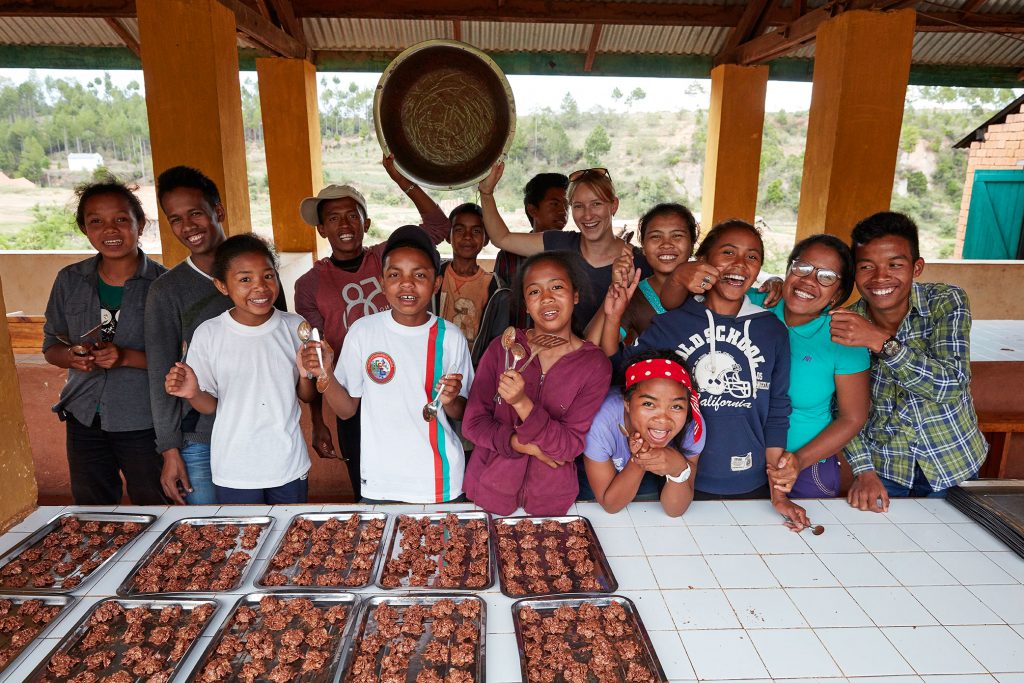 Eine Gruppe junger Madagassen hebt lächelnd einen leeren Topf in die Höhe. Vor ihnen liegen mehrere Bleche mit gebackenen Teilchen