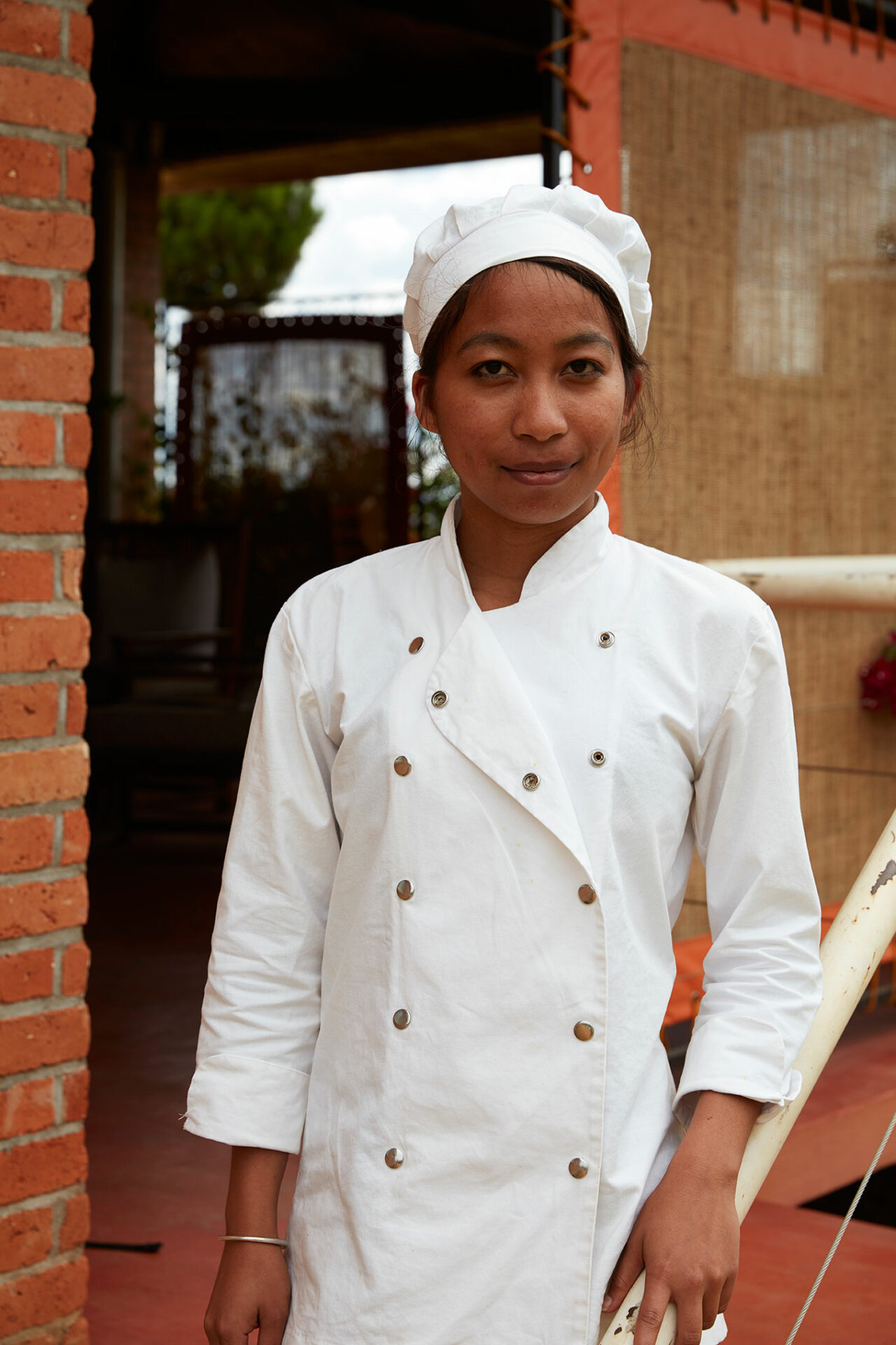 Eine junge madagassische Studentin steht in Kochbekleidung am Geländer einer Außentreppe und lächelt in die Kamera