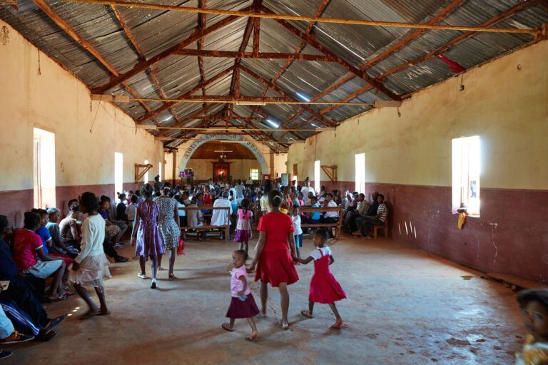 Madagassische Schüler sind in einer Kirche versammelt. Eine Schülerin hält zwei kleine Mädchen an den Händen