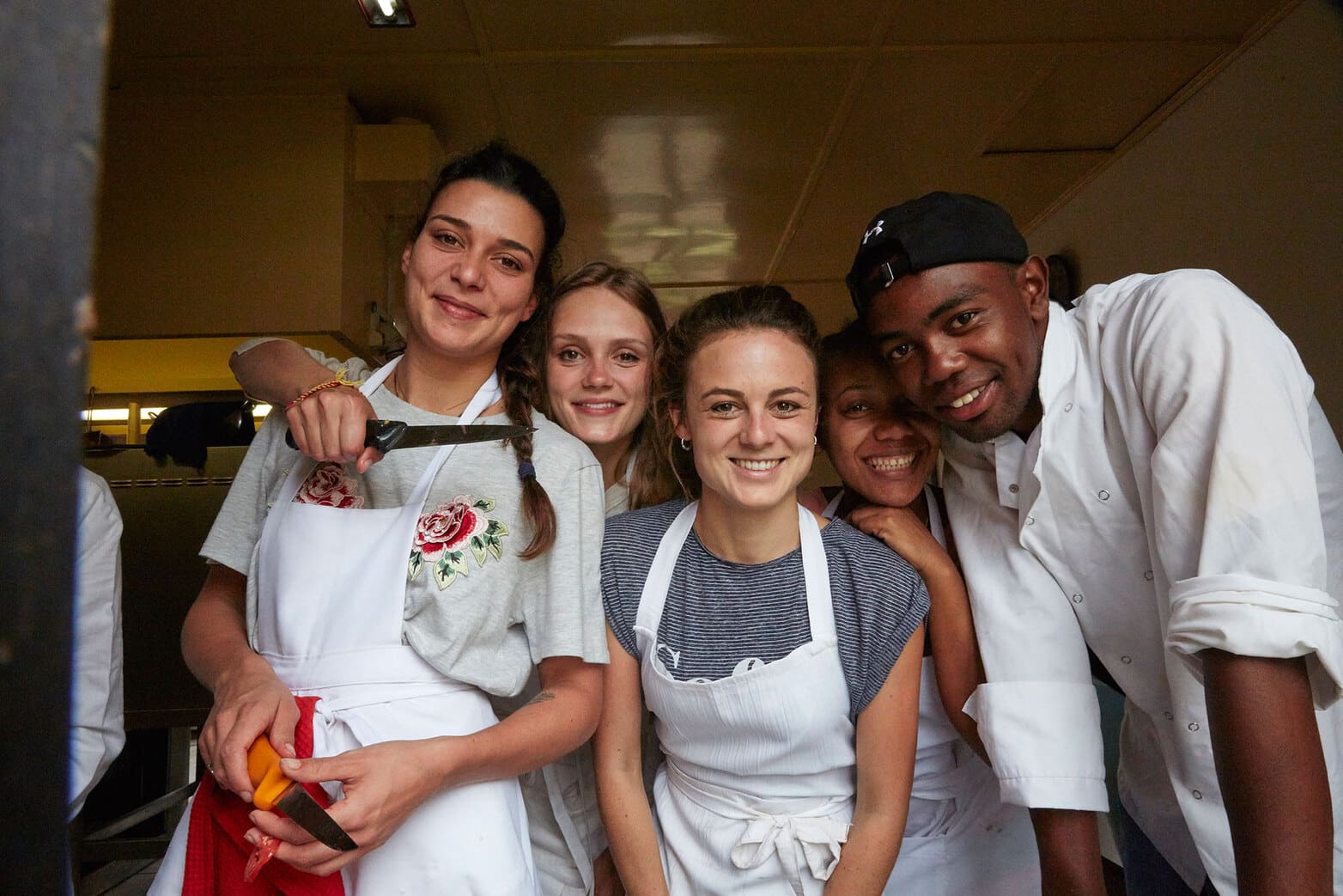 Madagassische Studenten und deutsche Volontärinnen kochen gemeinsam. Sie tragen Kochschürzen